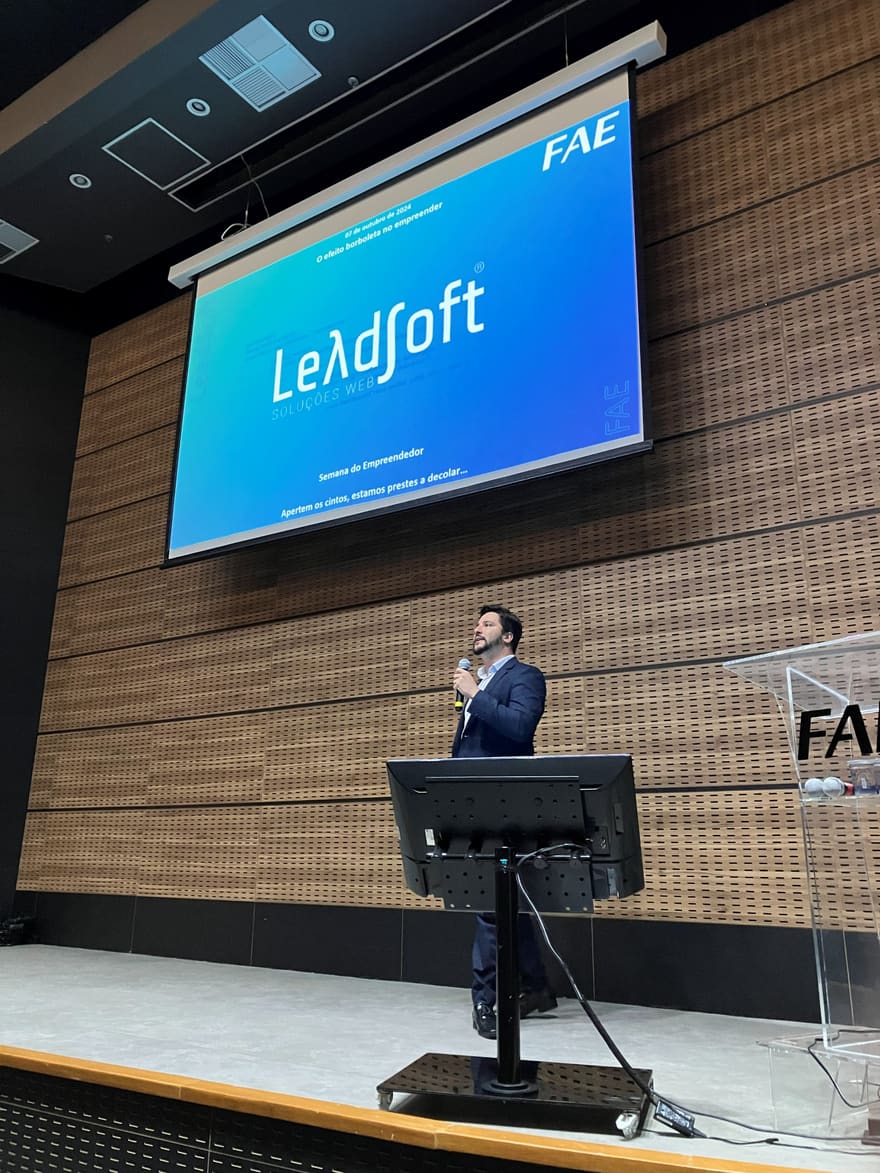 Lucas on the FAE stage, with the opening slide of the talk O efeito borboleta no empreender and the LeadSoft Soluções Web brand