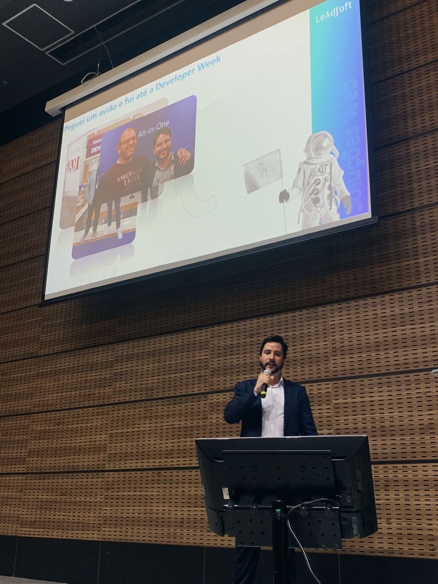 Lucas speaking into a microphone; the slide shows a photo with Oren Eini and the text I got on a plane and went to Developer Week